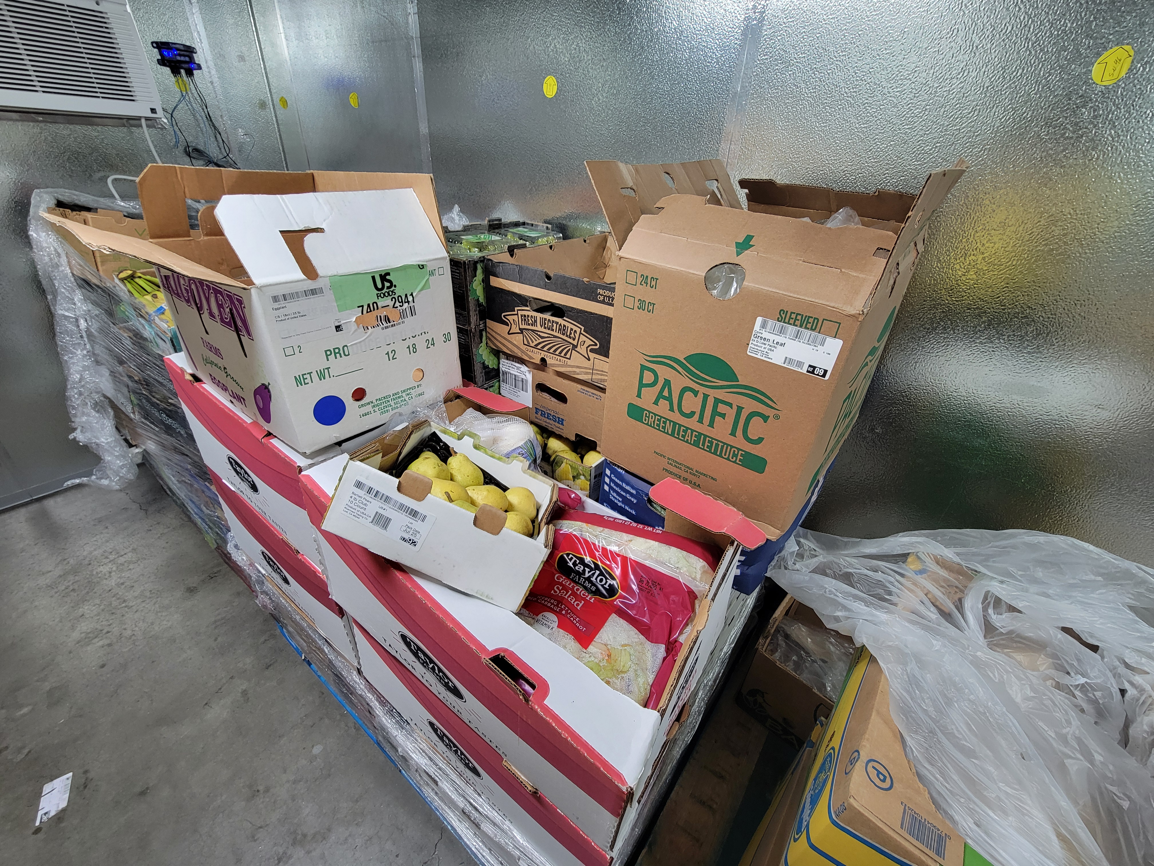 Three pallets of boxes of various produce in a fridge box unit.